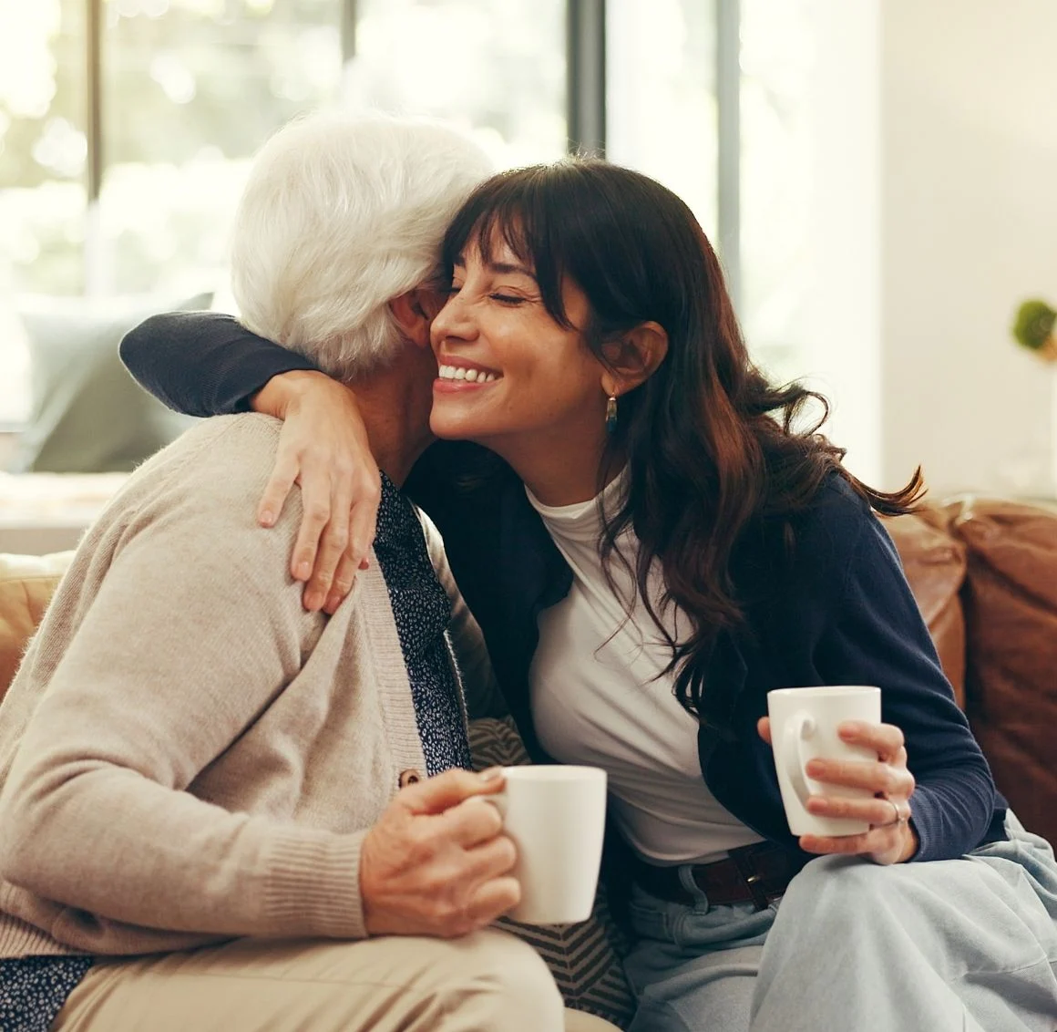 senior-woman-and-daughter-hugging-with-coffee-mugs